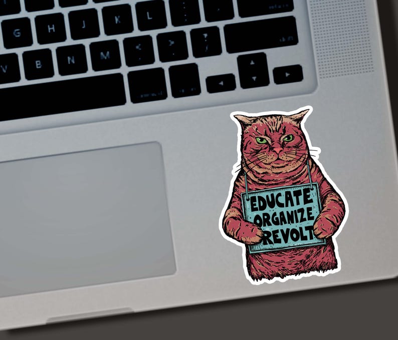 May include: A sticker featuring a red cat with green eyes holding a sign that reads "EDUCATE ORGANIZE REVOLT." The cat is on a laptop, and the sticker has a distressed, hand-drawn style.