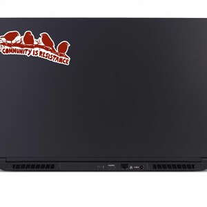 May include: A black laptop with a sticker featuring four red birds perched on a branch. The sticker also includes the text "COMMUNITY IS RESISTANCE" in red and white.