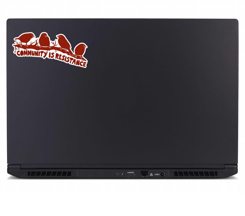 May include: A black laptop with a sticker featuring four red birds perched on a branch. The sticker also includes the text "COMMUNITY IS RESISTANCE" in red and white.