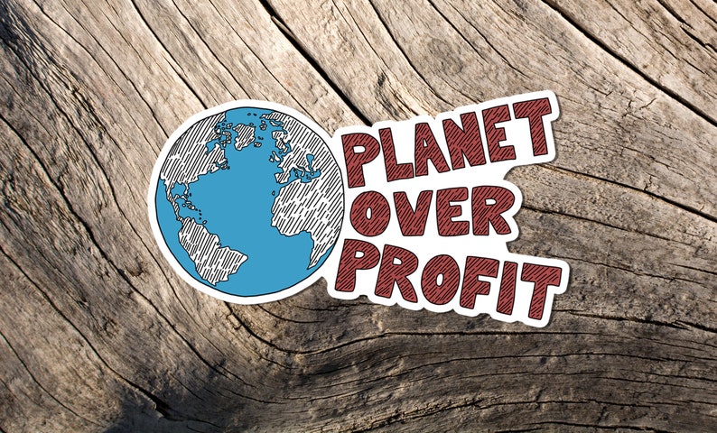 May include: A sticker with the words "PLANET OVER PROFIT" in maroon, with a blue and white globe illustration. The sticker is set against a weathered wood background, emphasizing an environmental theme.