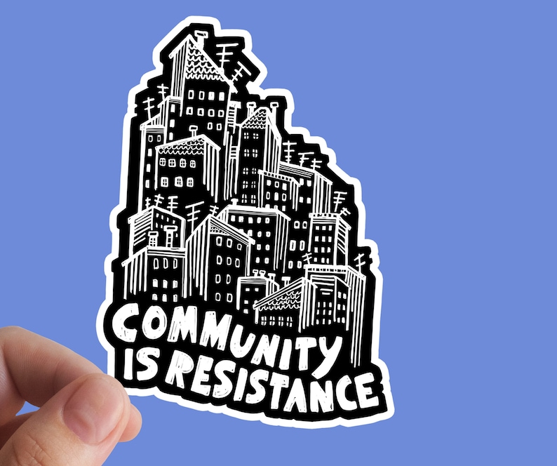 May include: A black and white sticker featuring a cityscape illustration. The buildings are densely packed with detailed windows, chimneys, and antennas. Bold text reads "COMMUNITY IS RESISTANCE" in a stylized font, set against a blue background.