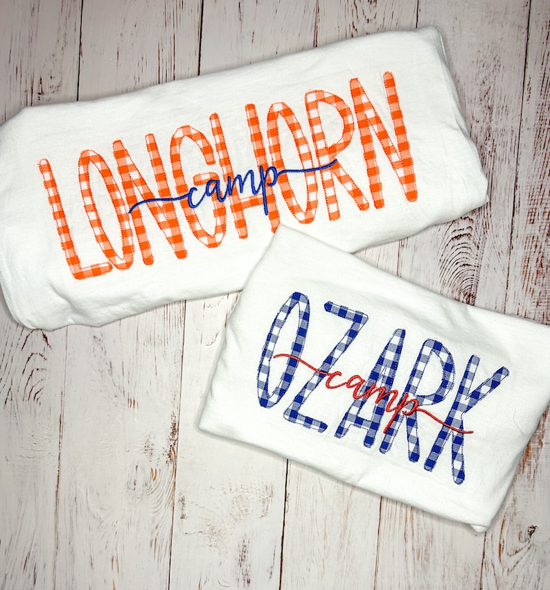 May include: Two white t-shirts with the words "Longhorn camp" and "Ozark camp" written in orange and blue checkered font.