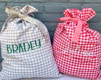 May include: Two personalised gift bags. One is tan and white gingham with "BRADEY" embroidered in green. The other is red and white gingham with "Julian" embroidered in white. Both bags have matching fabric ties.