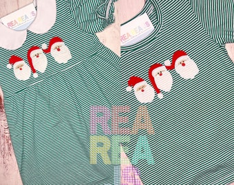 Puede incluir: Un vestido a rayas verdes y blancas y una camiseta a rayas verdes y blancas con caras de Papá Noel bordadas. El vestido tiene un cuello blanco Peter Pan. El texto "Rea Rea's" está en el cuello del vestido y la camiseta.