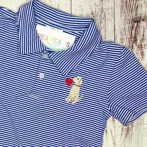 Pu&ograve; includere: Una polo a righe blu e bianche con una piccola immagine ricamata di un cane che tiene un cuore rosso. La polo ha un colletto e maniche corte.