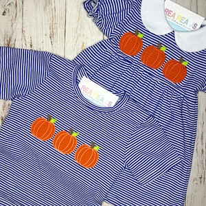 May include: Two blue and white striped shirts with embroidered pumpkins. The shirt on the left has three pumpkins and the shirt on the right has three pumpkins. The shirts have a white collar and are made by Rea Rea's.