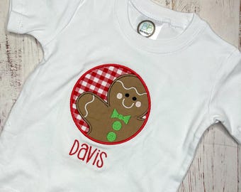 Puede incluir: Una camiseta blanca de manga corta con un aplique circular sobre un fondo de cuadros rojos y blancos. En el centro, un hombre de jengibre marrón con pajarita y botones verdes. El nombre Davis está bordado en rojo debajo del círculo.