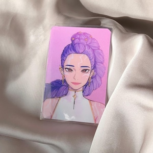 May include: A rectangular card featuring a stylized illustration of a woman with purple hair styled in an updo. The woman has gold earrings and a white top with gold accents. The background is pink.