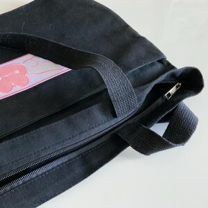 K&ouml;nnte beinhalten: Schwarze Canvas-Tragetasche mit einem rosa-wei&szlig;en Wolken-Patch und einem Rei&szlig;verschluss.