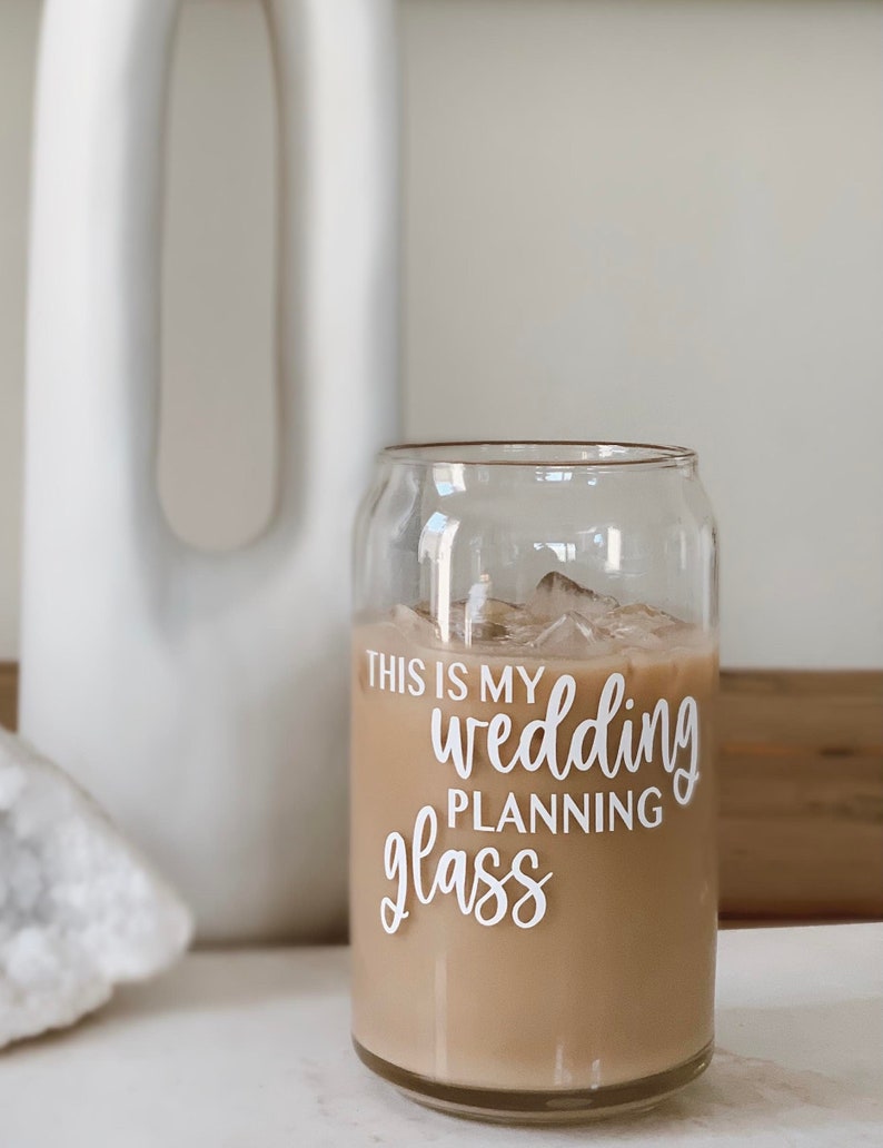 K&ouml;nnte beinhalten: Ein klares Glas mit einem braunen Getr&auml;nk und Eisw&uuml;rfeln. Auf dem Glas steht der Text "This is my wedding planning glass".