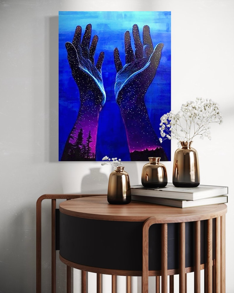 May include: A painting of two hands reaching up towards a blue sky with stars. The hands are filled with stars and the sky is a deep blue. The painting is on a canvas and is framed.