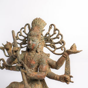 May include: A bronze statue of a Hindu deity with multiple arms, holding various objects. The statue is weathered and has a green patina. The deity is wearing a crown and has a detailed headdress.