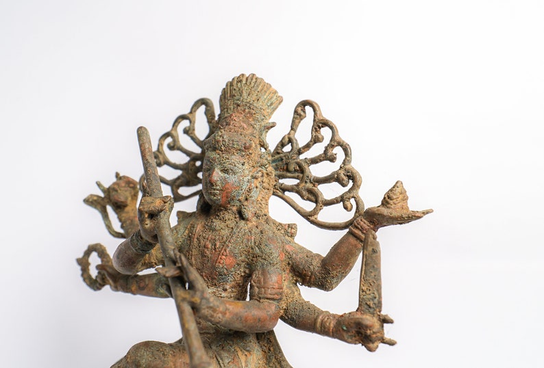 May include: A bronze statue of a Hindu deity with multiple arms, holding various objects. The statue is weathered and has a green patina. The deity is wearing a crown and has a detailed headdress.