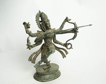 May include: A green bronze statue of a Hindu deity with multiple arms holding a bow and arrow. The deity is standing on a circular base with intricate designs.