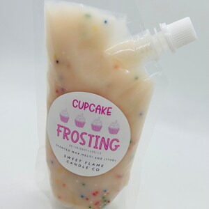 Op de afbeelding: Een witte zak met een roze en wit label waarop "Cupcake Frosting" staat met drie cupcake-afbeeldingen. Het label vermeldt ook "Scented Wax Melt - 6 oz (170g) Sweet Flame Candle Co."