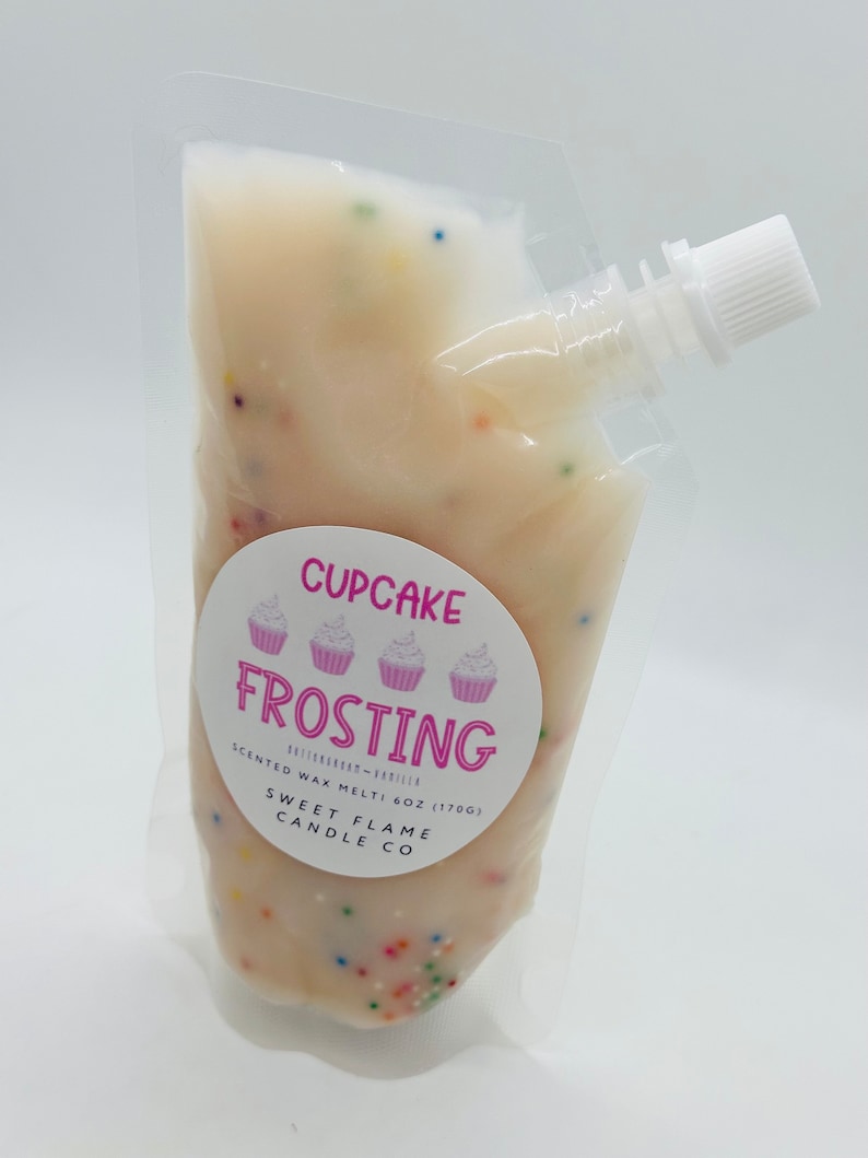 Op de afbeelding: Een witte zak met een roze en wit label waarop "Cupcake Frosting" staat met drie cupcake-afbeeldingen. Het label vermeldt ook "Scented Wax Melt - 6 oz (170g) Sweet Flame Candle Co."