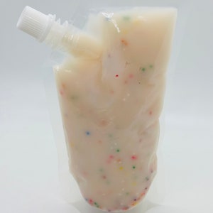 Op de afbeelding: Een doorzichtige plastic zak gevuld met een witte romige substantie met kleurrijke sprinkels. De zak heeft een witte tuit.