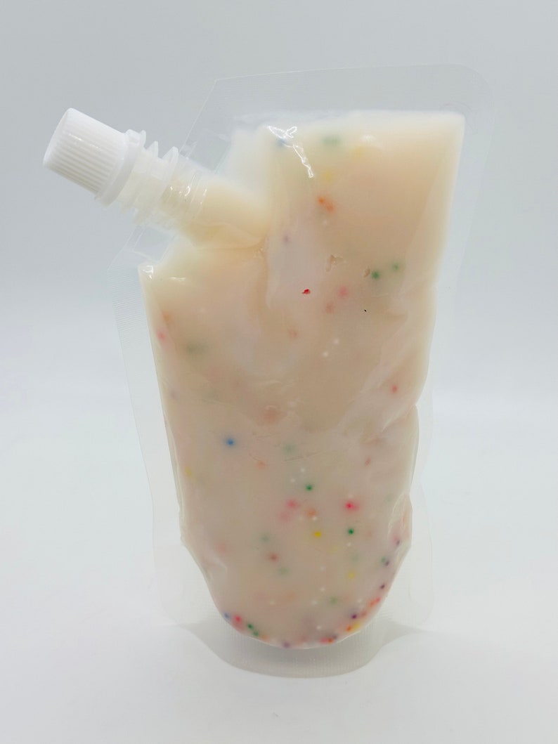 Op de afbeelding: Een doorzichtige plastic zak gevuld met een witte romige substantie met kleurrijke sprinkels. De zak heeft een witte tuit.