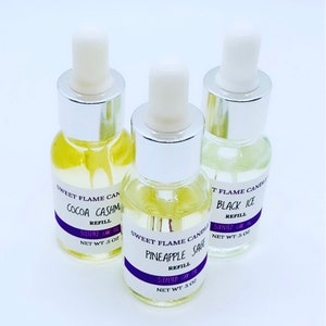 May include: Three glass bottles with dropper tops filled with clear liquid. The bottles are labeled with the text "Sweet Flame Candles" and the names of the scents: "Cocoa Cashmere", "Pineapple Sage", and "Black Ice". Each bottle is labeled "Scented Oil Refill" and has a net weight of 5 oz.