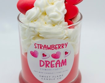 May include: A pink soy wax candle with a white whipped cream topping and red heart decorations. The label reads "Strawberry Dream" and "Sweet Flame Candle Co."