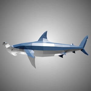 May include: A low-poly geometric sculpture of a hammerhead shark. The figure is constructed from flat, angular blue and white panels, creating a faceted, three-dimensional representation of the marine creature with a distinct wide head.