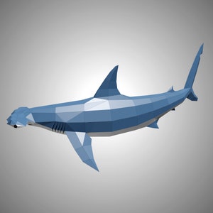 May include: A low-poly geometric sculpture of a hammerhead shark. The shark is constructed from flat, angular blue and light gray panels, creating a faceted, three-dimensional appearance with a distinct wide head, dorsal fin, and tail.