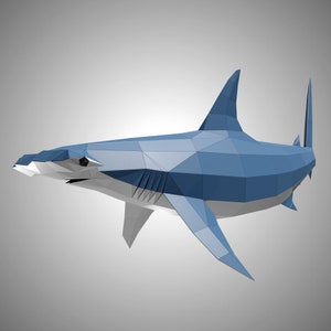 May include: A low-poly geometric hammerhead shark sculpture featuring a blue upper body and a white underbelly. The shark is constructed from flat, angular planes that create a faceted, three-dimensional appearance with a distinct wide head.
