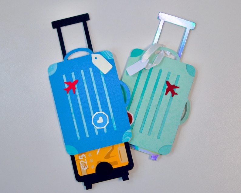 May include: Two decorative suitcase-shaped gift card holders. One is blue with a red airplane and white stripes, the other is mint green with a red airplane and white stripes. Each has a pull-out drawer.