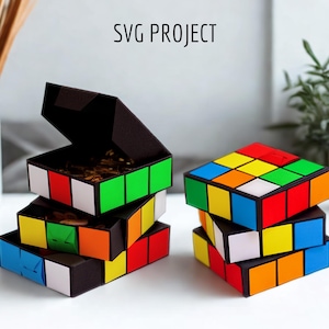 May include: Stack of three open, cube-shaped boxes with colorful squares, resembling a Rubik's Cube. The boxes are black with red, white, green, orange, yellow, and blue squares. The text "SVG PROJECT" is at the top.