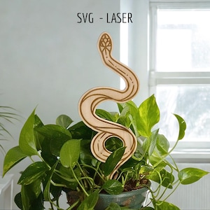 May include: A wooden snake plant stake with etched details, placed in a pot of green plants. The stake features a stylized snake design with a detailed head and body markings. The text "SVG - LASER" is in the top left corner.