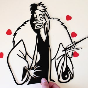 May include: A black and white paper cut-out of Cruella De Vil from the Disney film 101 Dalmatians. She is wearing a fur coat and holding a cigarette. There are five red hearts in the background.