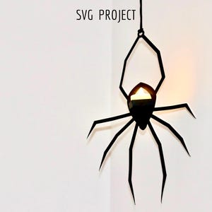 May include: Black metal spider silhouette hanging from the ceiling with a candle inside the body.  "SVG PROJECT" is written above the spider.