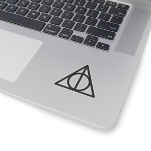 May include: A black and white sticker of the Deathly Hallows symbol from the Harry Potter series. The symbol is a triangle with a circle inside, and a vertical line through the circle.