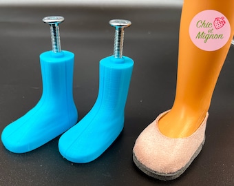 May include: Two pairs of blue plastic doll shoes with silver screws. The shoes are designed to be attached to a doll's feet. The shoes are on a white surface. Chic et Mignon is written on a pink circle with a strawberry.