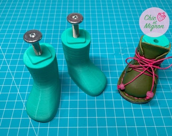 May include: Three shoe forms, two are teal green 3D printed forms with a screw in the top, and one is a green leather shoe with pink laces and pink beads.