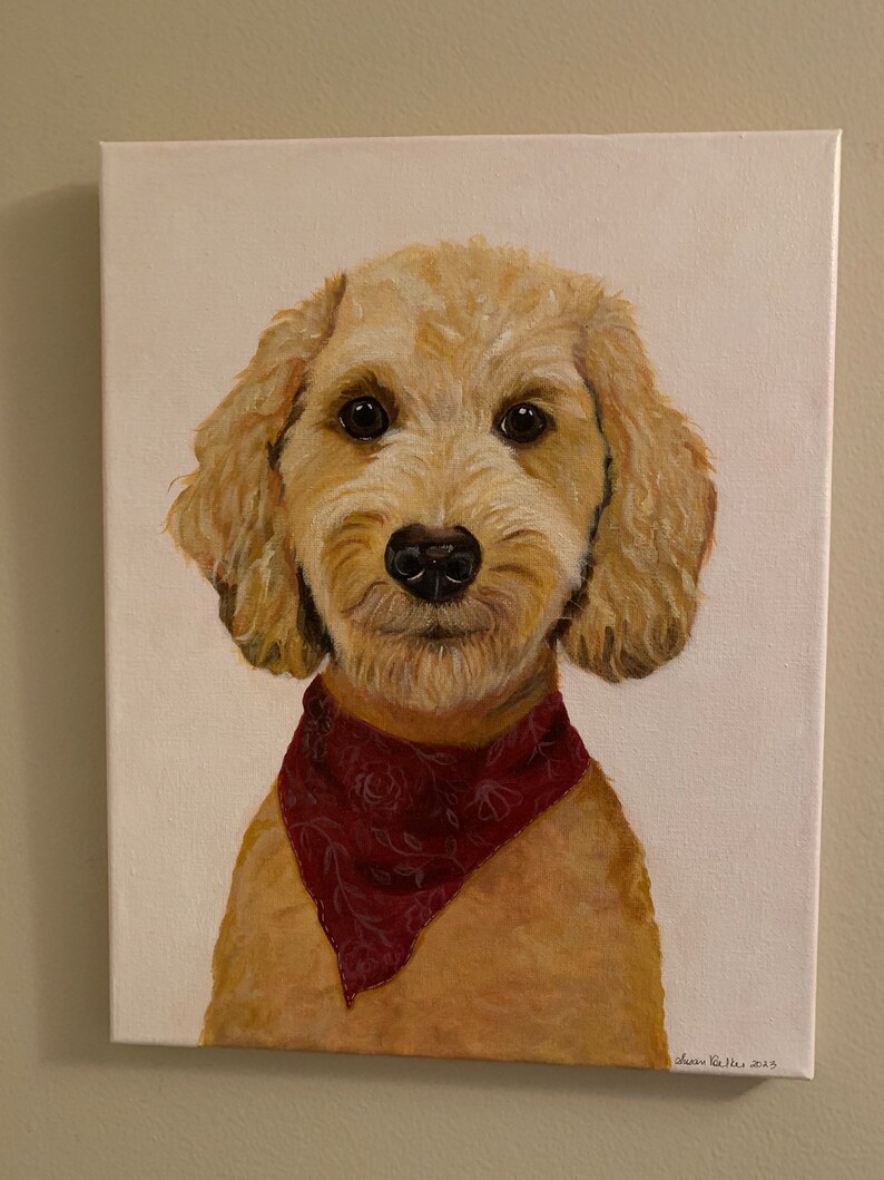 May include: A canvas painting of a golden doodle dog with a red bandana. The dog has brown eyes and a black nose. The painting is signed in the bottom right corner. The background is white.