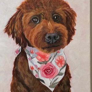 May include: A portrait of a brown dog with a floral bandana. The dog has dark eyes and a black nose. The bandana is white with pink and red roses and green leaves. The painting is on a canvas with a light pink background.
