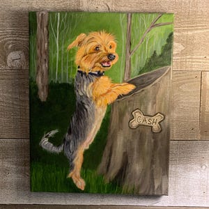 May include: A painted canvas depicts a Yorkshire Terrier dog with tan and gray fur, standing on its hind legs next to a tree stump. The dog is wearing a black collar. The tree stump has a bone-shaped sign that reads "CASH". The background shows a green forest.