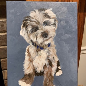 May include: A painted portrait of a dog with a blue and grey background. The dog has a mix of white, brown, and black fur, with one blue eye and one brown eye. It wears a blue collar with a tag. The artwork is on a canvas.