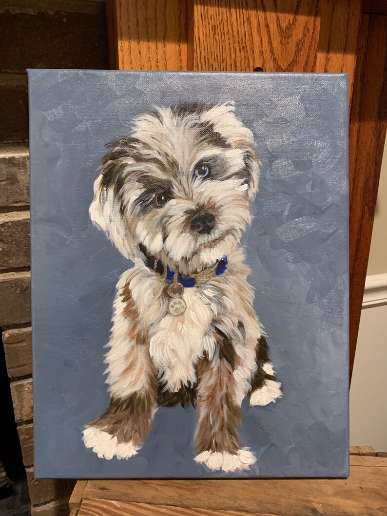 May include: A painted portrait of a dog with a blue and grey background. The dog has a mix of white, brown, and black fur, with one blue eye and one brown eye. It wears a blue collar with a tag. The artwork is on a canvas.