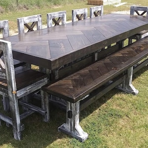 May include: A dining set featuring a large rectangular table and a long bench with dark brown wood tops arranged in a herringbone pattern. The table and bench bases, along with the matching chairs, have a distressed white and black finish.