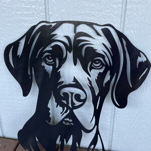 May include: Black metal silhouette of a dog's head, with a detailed face and floppy ears. The silhouette is cut out of metal and has a rustic, industrial look.