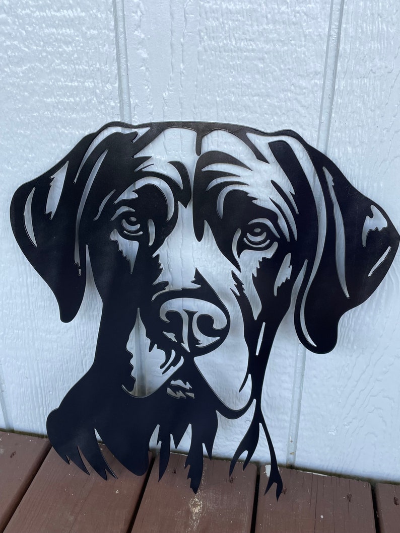May include: Black metal silhouette of a dog's head, with a detailed face and floppy ears. The silhouette is cut out of metal and has a rustic, industrial look.