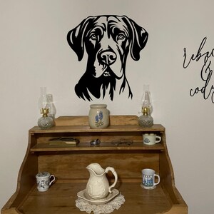 May include: A black and white silhouette of a dog's head with the names "Rebecca & Cody" written in cursive on a white wall. A wooden shelf with two oil lamps, a pitcher, and mugs is in the foreground.