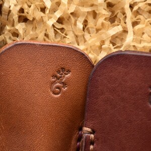 May include: Close-up of several leather items in shades of brown, each with a small embossed lizard design. The items are nestled in a wooden box filled with shredded paper. The leather has a textured appearance.