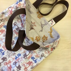 Puede incluir: Una bolsa de mano marrón con un forro de tela blanco. El exterior de la bolsa presenta un patrón de scooters rojos, azules y grises. El interior de la bolsa presenta un patrón de animales marrones y blancos. La bolsa tiene asas marrones.