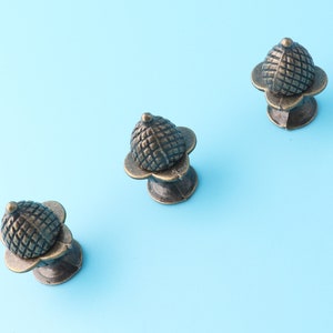 May include: Three antique bronze cabinet knobs with a decorative, geometric design. Each knob has a round, textured top and a base with four petals.