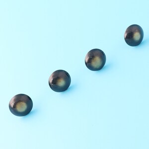 Könnte beinhalten: Vier runde Knöpfe in Schwarz und Gold mit glänzender Oberfläche. Die Knöpfe sind in einer Reihe auf einem hellblauen Hintergrund angeordnet.