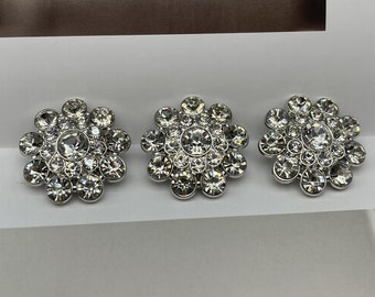 May include: Three silver-toned brooches with a flower design. Each brooch is made of a cluster of small, clear rhinestones.