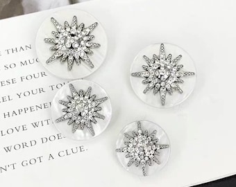 May include: Four white round buttons with a silver starburst design. Each starburst is made of rhinestones.